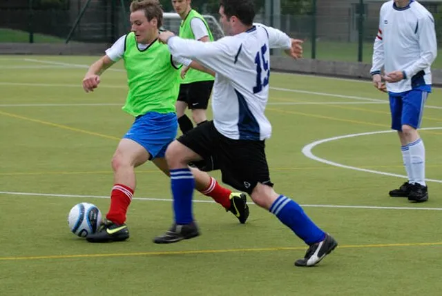 Two players challenging for the ball during a five-a-side match, demonstrating how to tackle in football by timing a standing challenge and positioning the body to win possession.