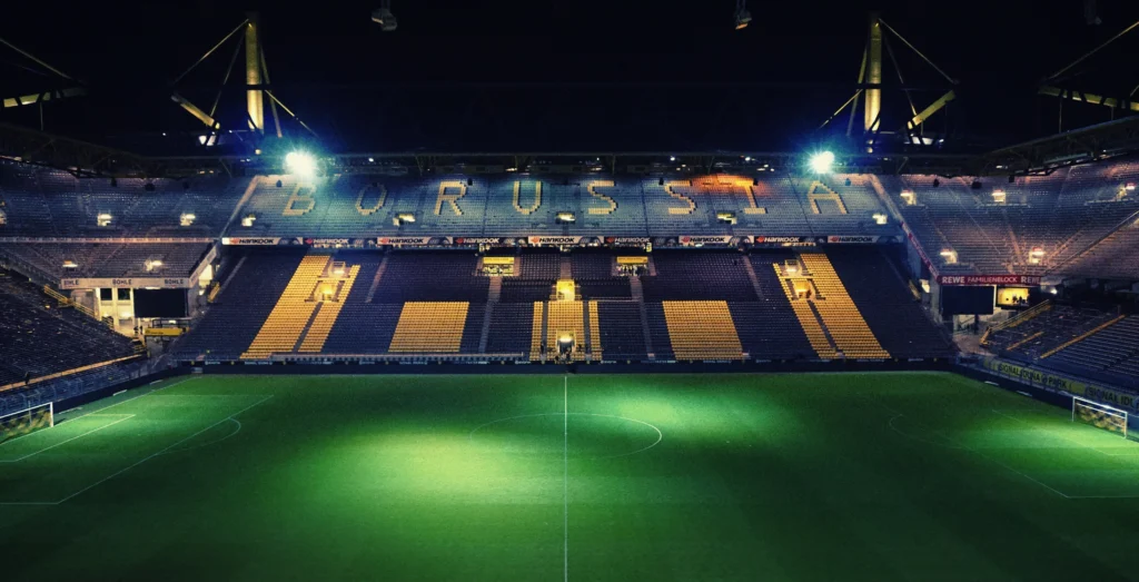 Large football stadium with illuminated pitch at night illustrating the question are football pitches the same size.