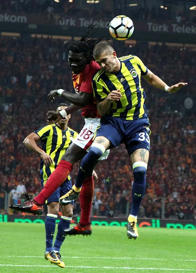 Two professional football players leap to head the ball during a match, clearly showing the aerial threat meaning in football as attackers and defenders battle in the air.