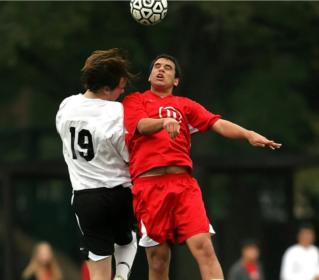 Two football players jumping high for a header, illustrating the vertical power and athletic strength used to win aerial duels.