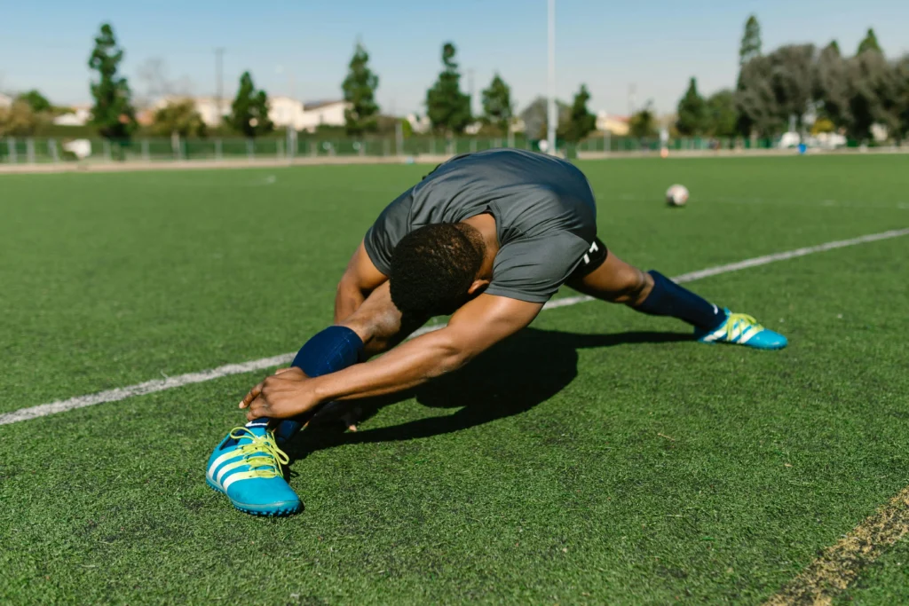 Football player stretching on a grass pitch before training, demonstrating why flexibility is important in football for injury prevention, mobility, and performance.