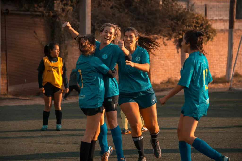 Women football players celebrating together after a goal, illustrating the spine of a football team.